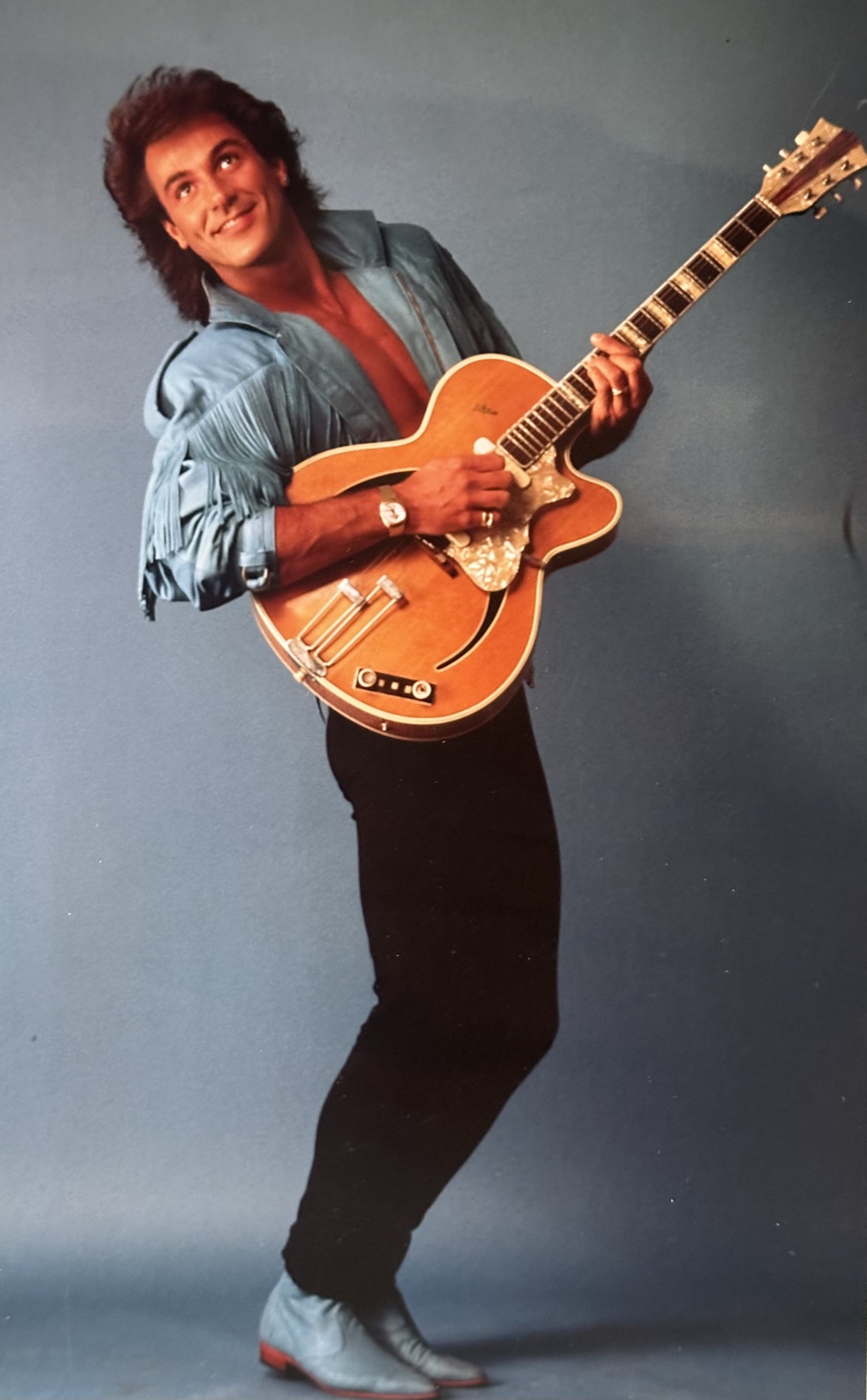 Studio photograph of a singer-songwriter holding a guitar upright